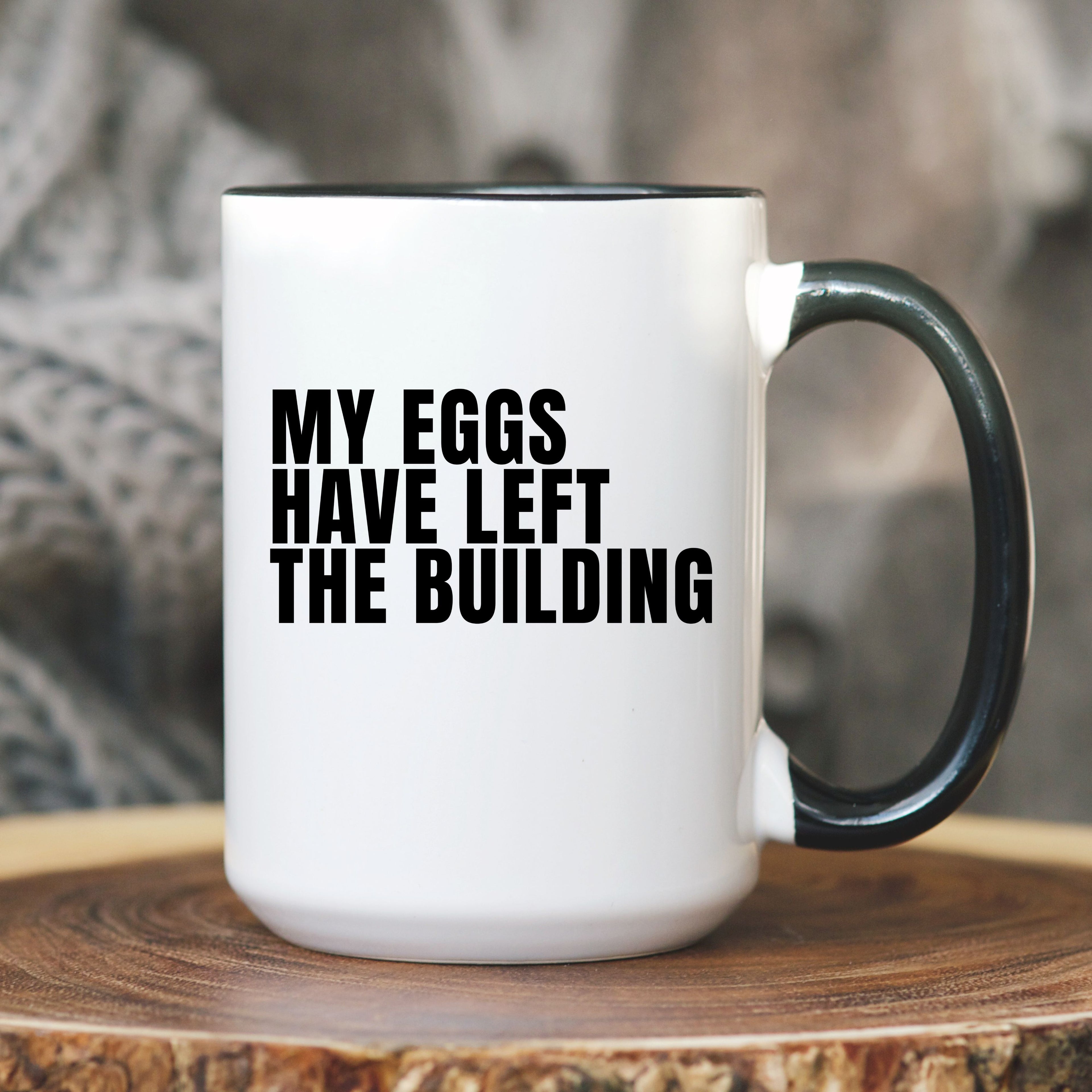 White mug with black text 'MY EGGS HAVE LEFT THE BUILDING' on a wooden surface.